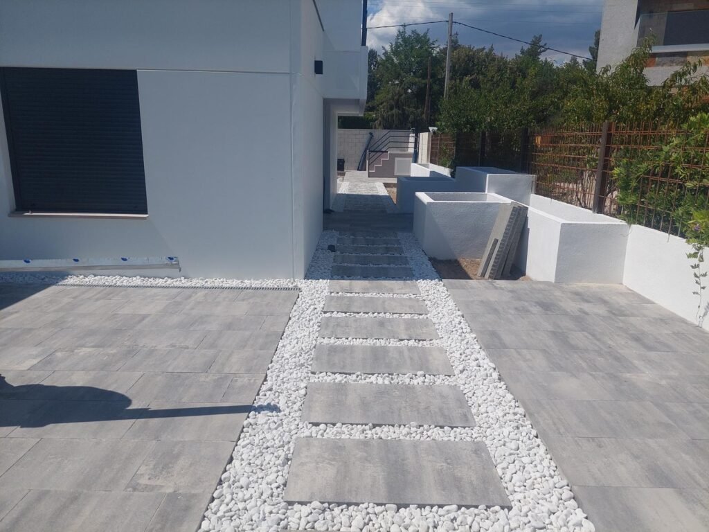 Exterior moderno con pavimento porcelánico y camino de grava blanca en vivienda unifamiliar